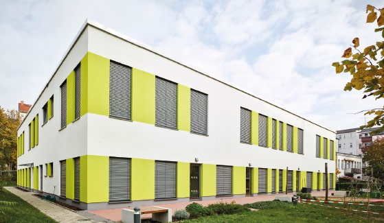 Modernes zweistöckiges Gebäude mit weißer Fassade und senkrechten grünen Streifen sowie mehreren Fensterläden